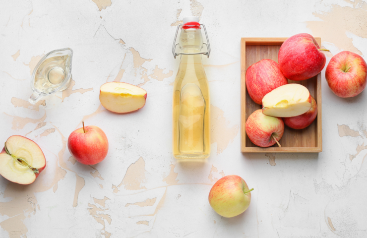 Flasche mit Apfelessig und ganzen und halbierten Äpfeln