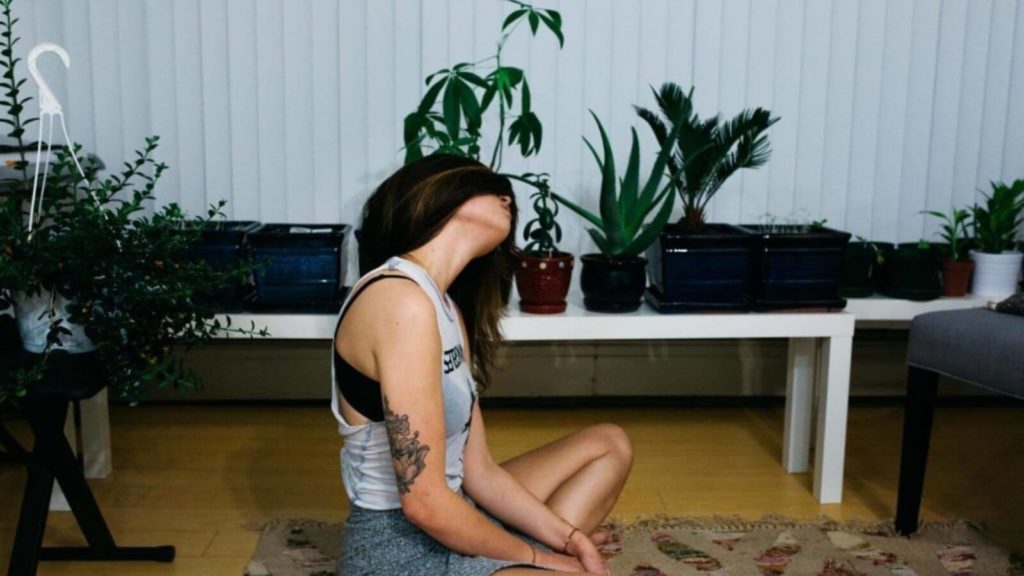 Frau macht Yoga im eigenen Wohnzimmer zur Stressbewältigung