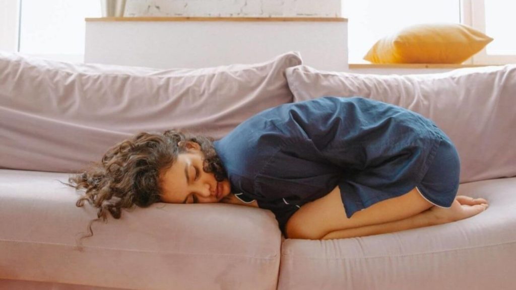 Frau liegt verkrampft auf Sofa wegen Darmproblemen.